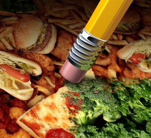 Unhealthy or healthy choice and changing your diet revising bad eating habits with an image of greasy fat fast food being erased by a pencil revealing underlying healthy green vegetables as a concept for good nutrition lifestyle changes.